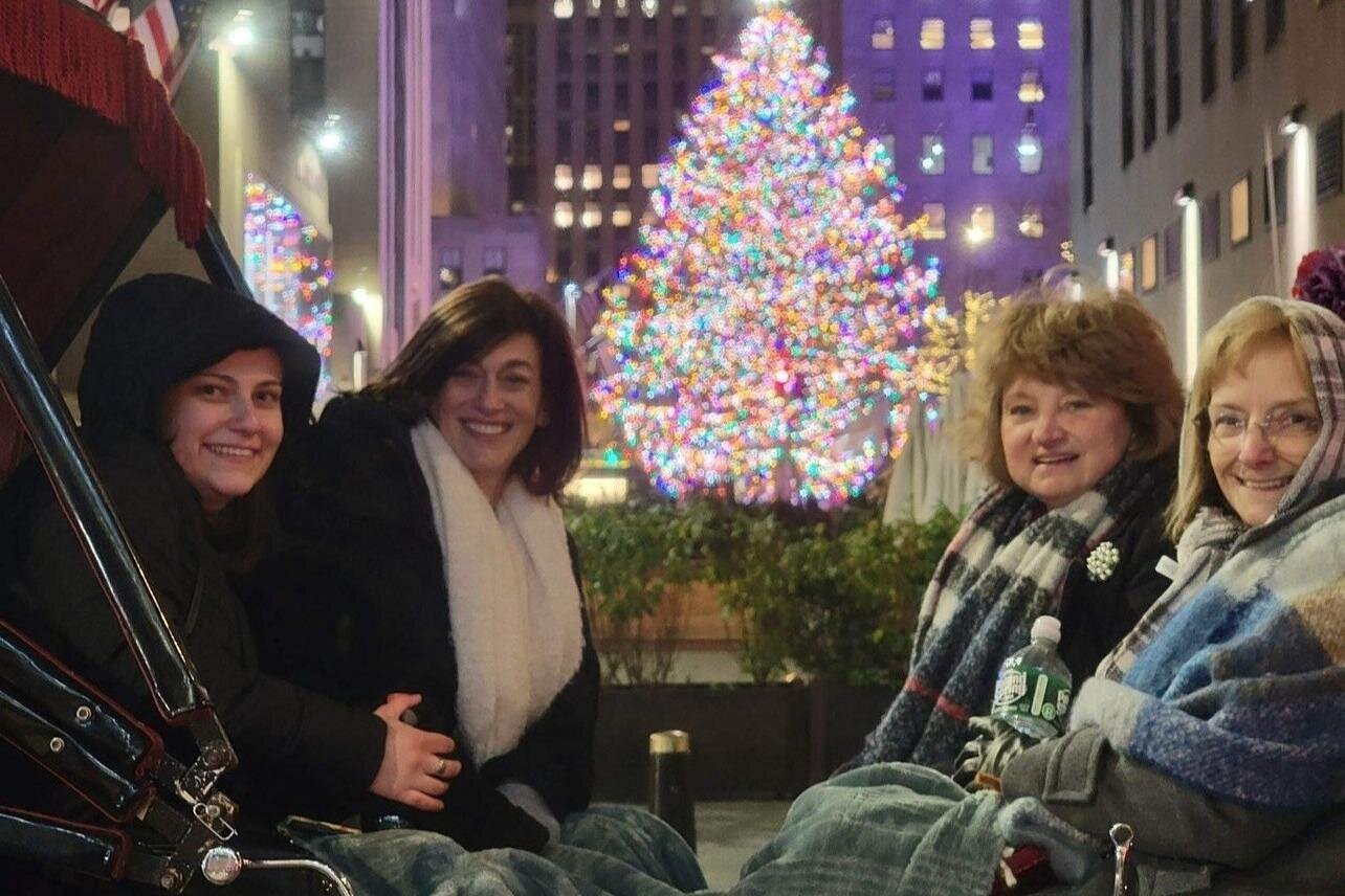 Vier Frauen sitzen während einer winterlichen Kutschfahrt in New York vor einem bunt beleuchteten Weihnachtsbaum.