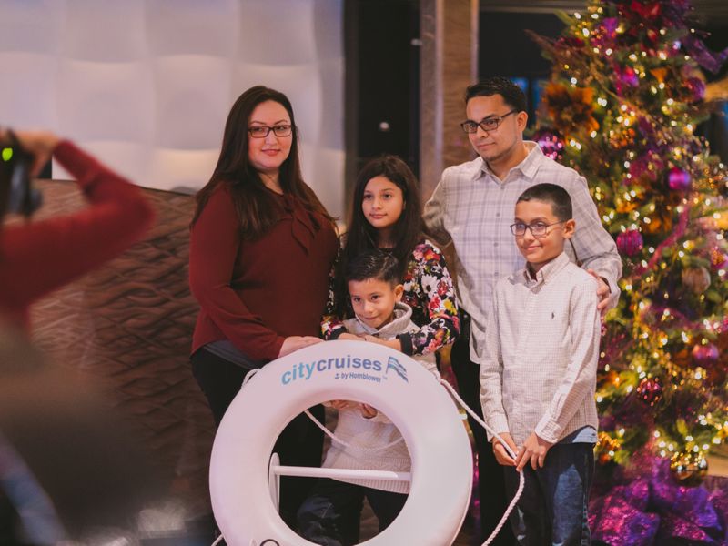 Familie posiert vor einem geschmückten Weihnachtsbaum mit einem City-Cruises-Rettungsring während einer festlichen Schifffahrt.
