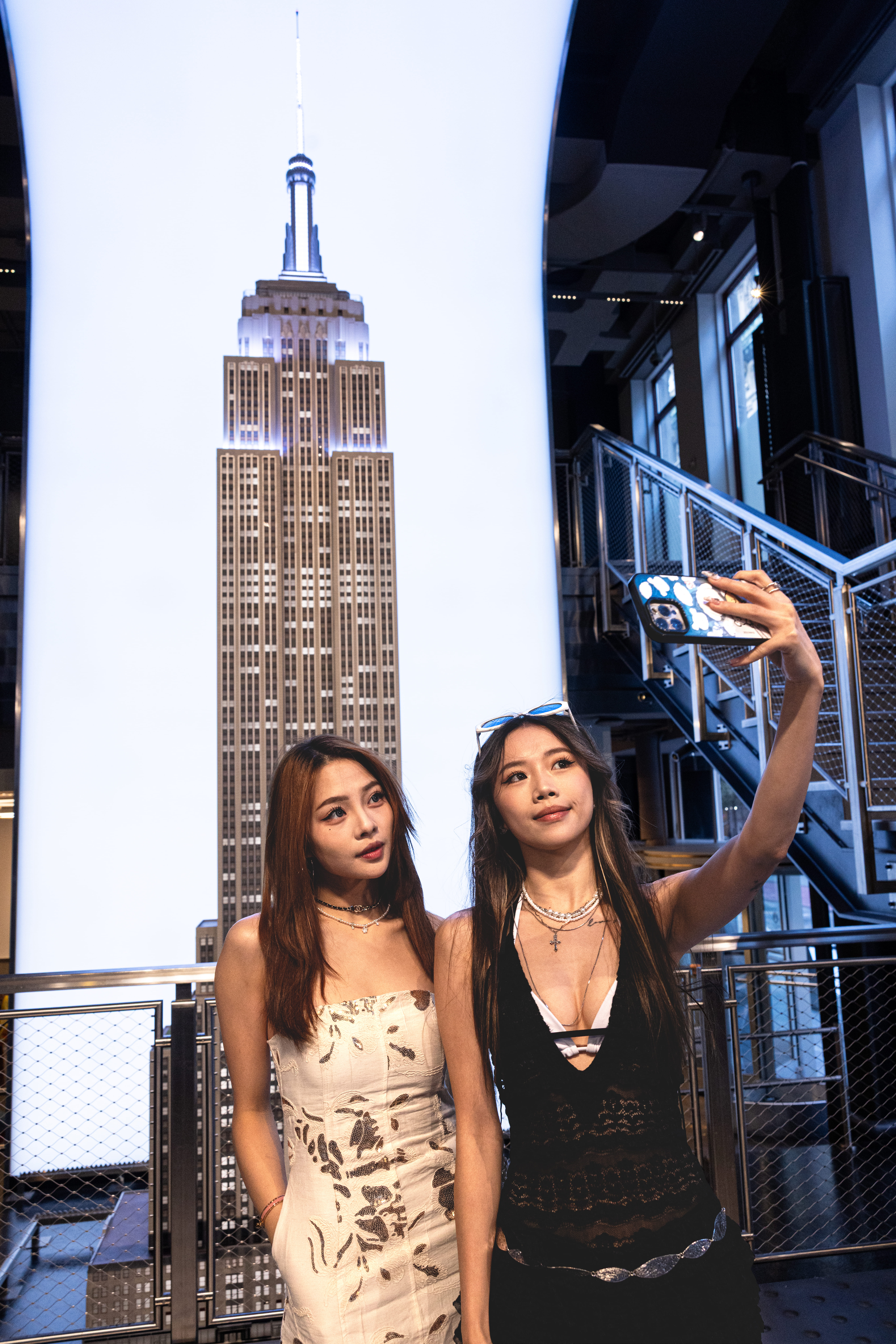 Zwei Besucherinnen machen ein Selfie vor einer großen Darstellung des Empire State Buildings im Observatory in New York.