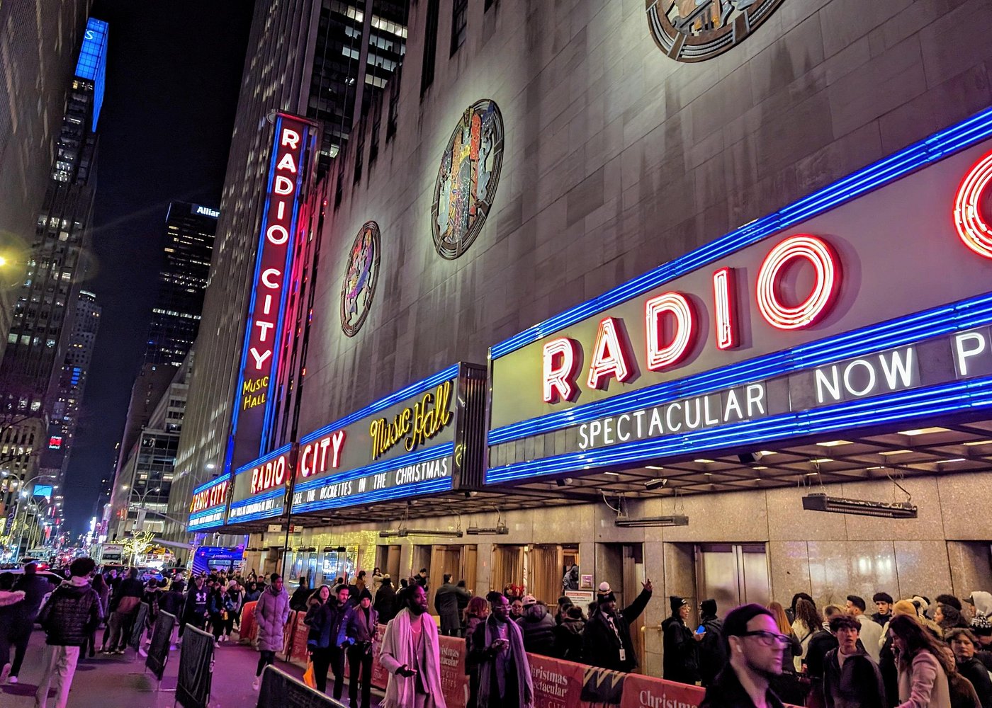 Beleuchtete Leuchtreklame der Radio City Music Hall in Manhattan mit Besuchern vor dem berühmten Veranstaltungsgebäude.