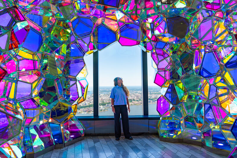 Besucherin in einer farbenfrohen, kristallartigen Installation mit Ausblick auf New York.