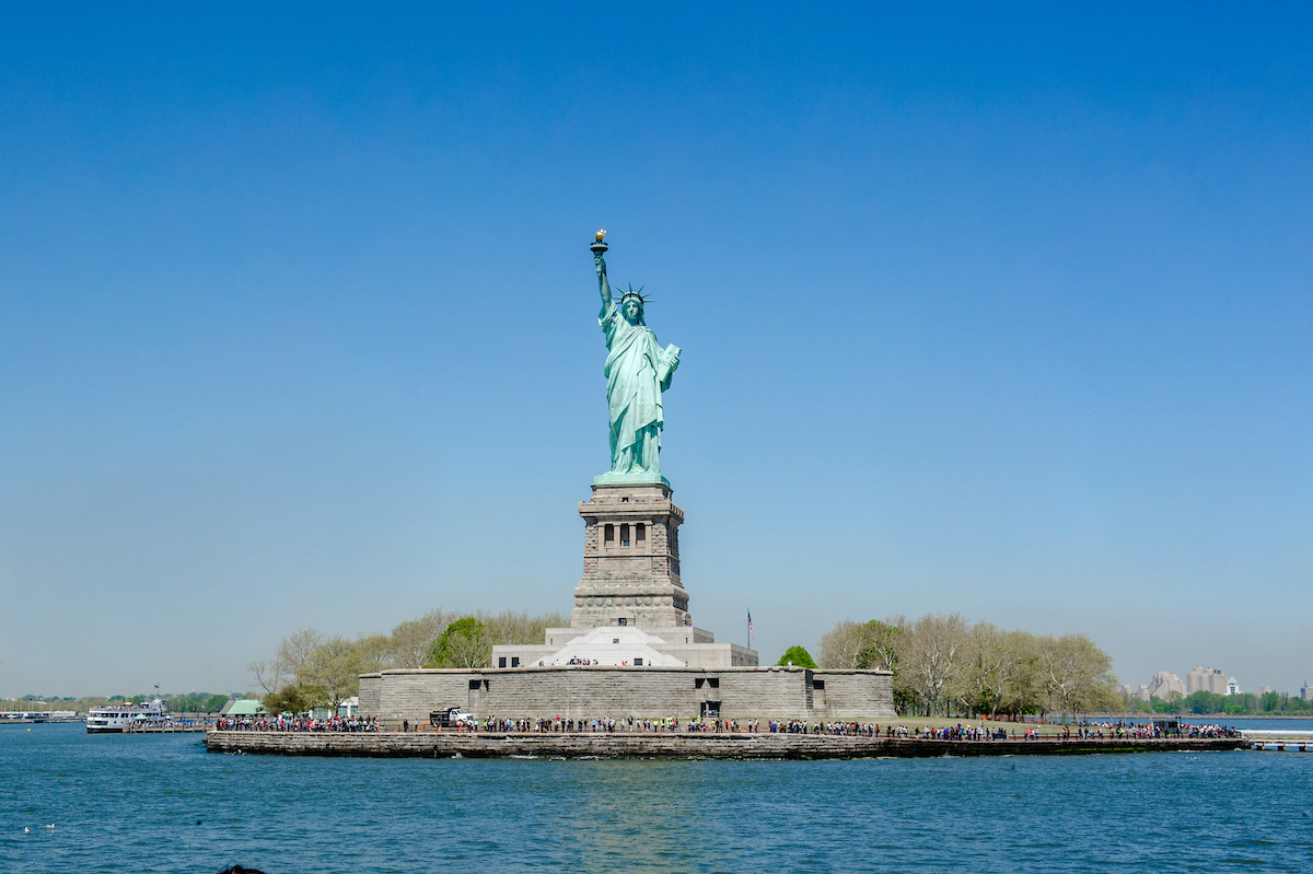 Freiheitsstatue in Frontalansicht auf Liberty Island vor blauem Himmel