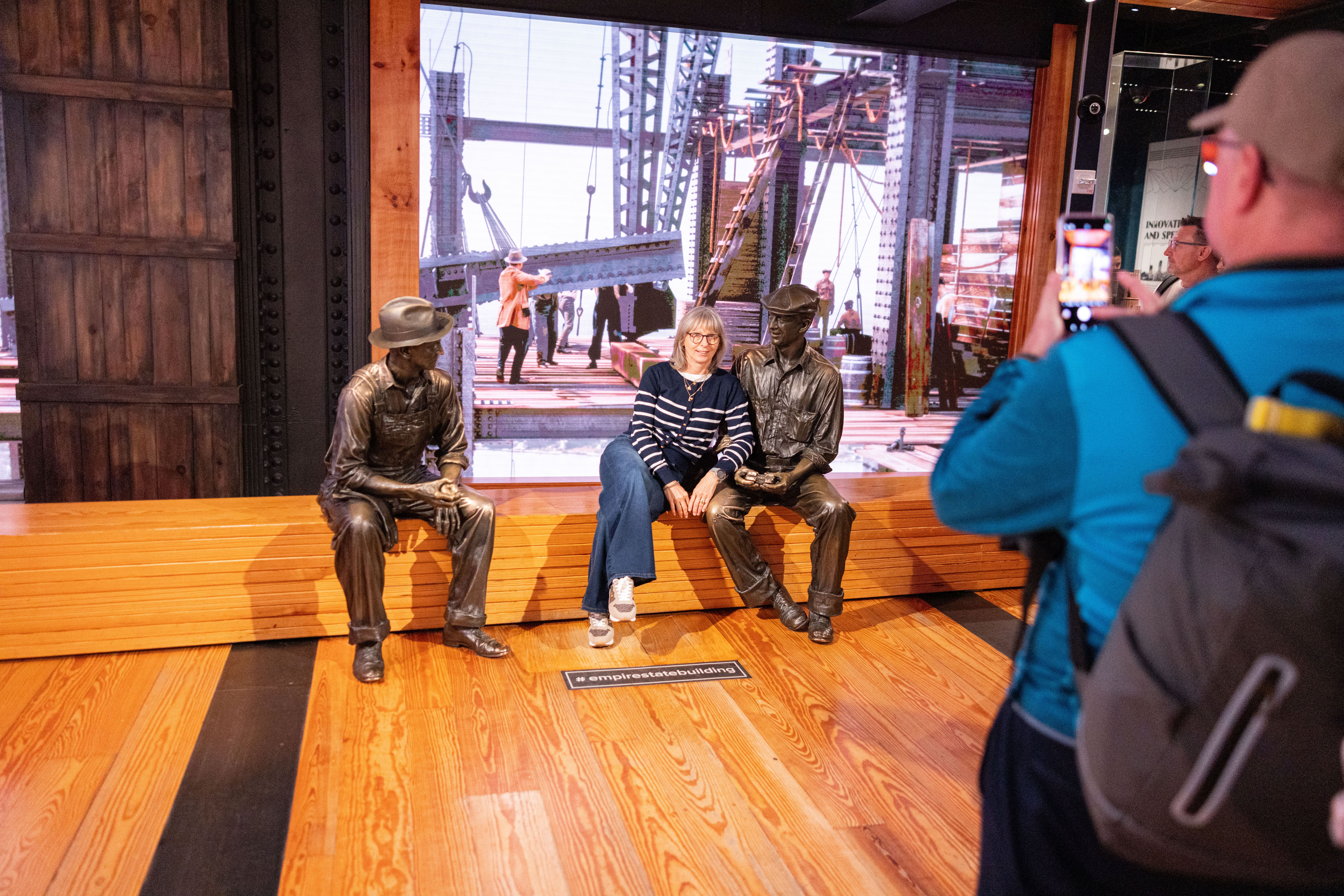Besucherin posiert zwischen Figuren von Bauarbeitern in der Ausstellung zur Entstehung des Empire State Buildings