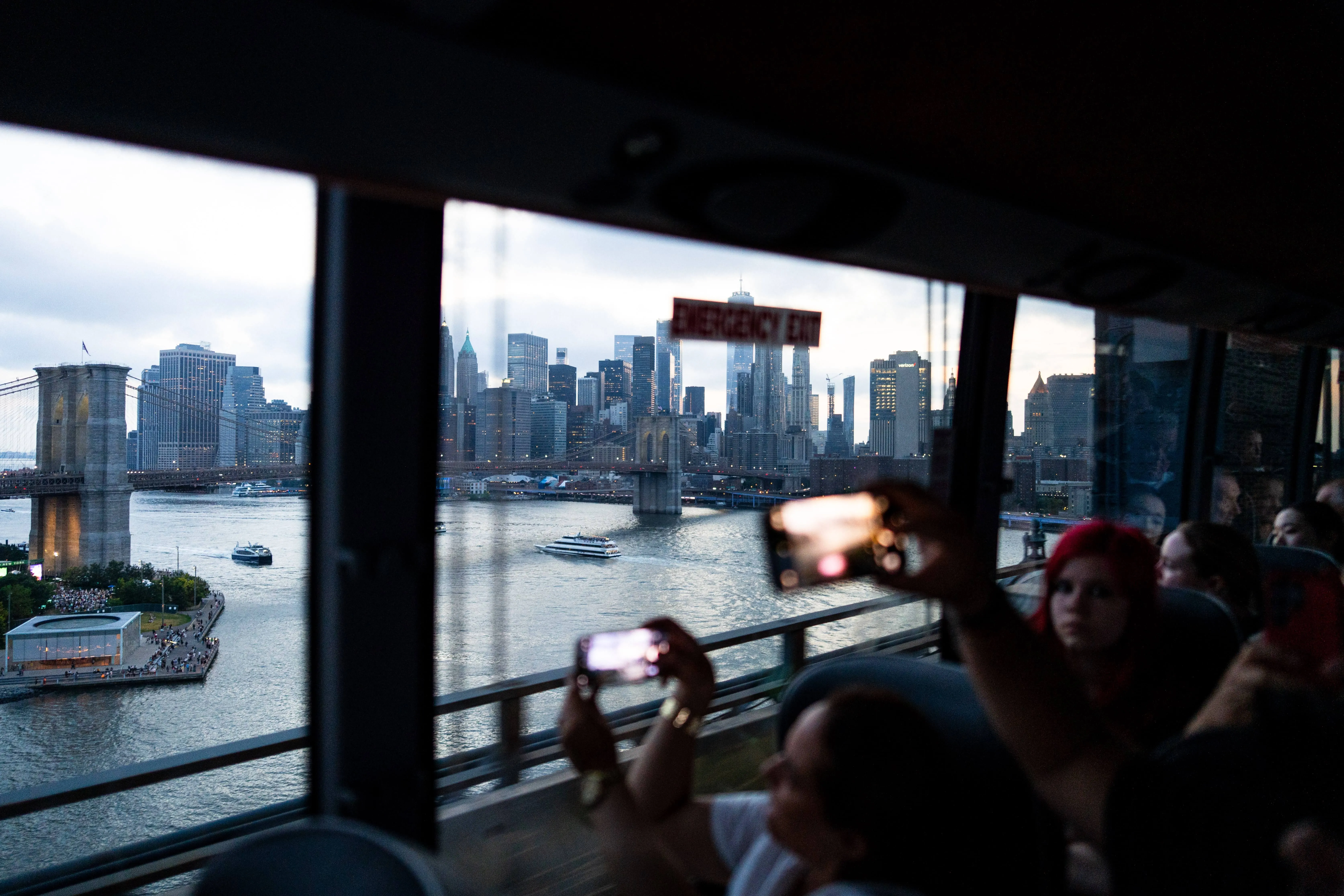 Touristen fotografieren die Brooklyn Bridge und die Skyline von Manhattan vom Oberdeck eines Sightseeing-Busses aus bei Abenddämmerung