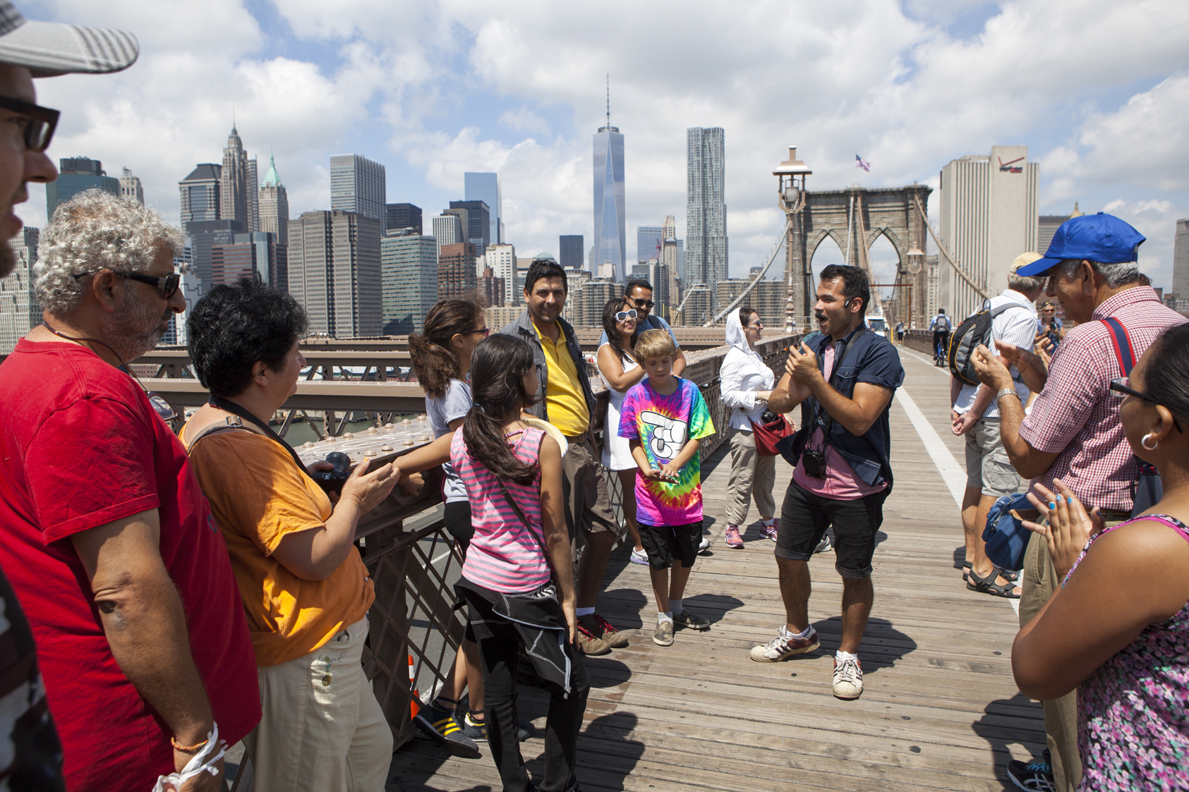 Ein Tourguide erklärt einer aufmerksamen Gruppe von Besuchern auf dem Holzsteg der Brooklyn Bridge spannende Details zur Stadtgeschichte.