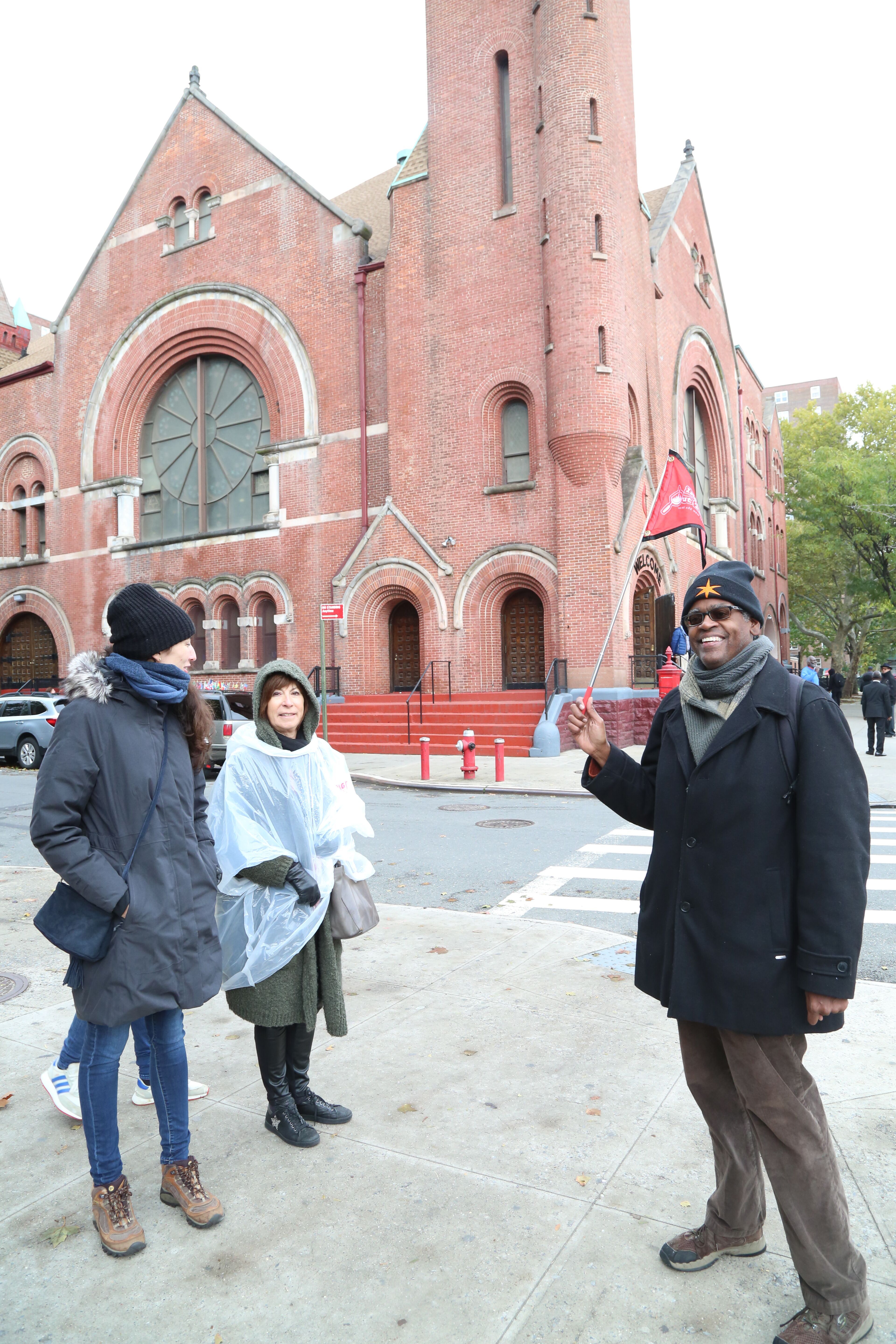 Tour-Guide mit Besucherinnen vor einer historischen Kirche in Harlem, New York