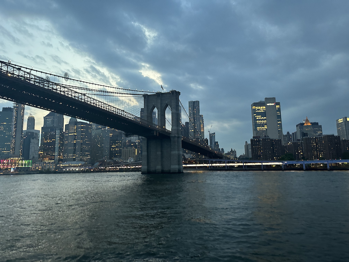 Brooklyn Bridge beleuchtet bei Abenddämmerung vor der Skyline von Manhattan