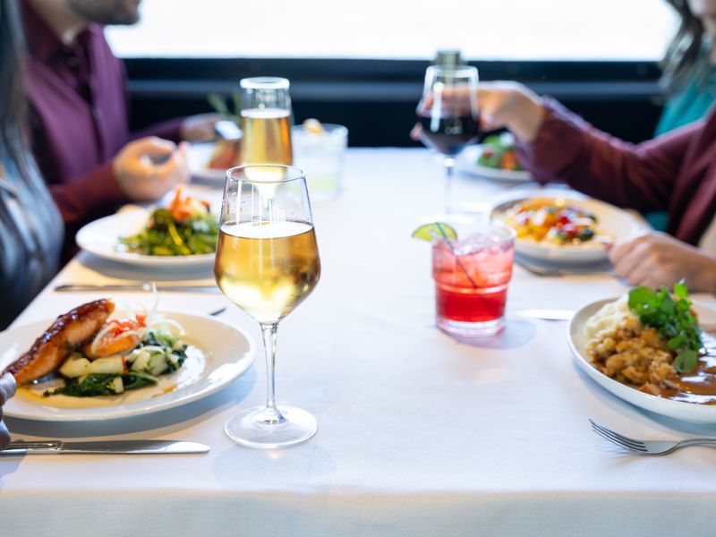 Gedeckter Tisch auf der Dinner Cruise mit Weingläsern, Cocktail und mehreren servierten Hauptgerichten