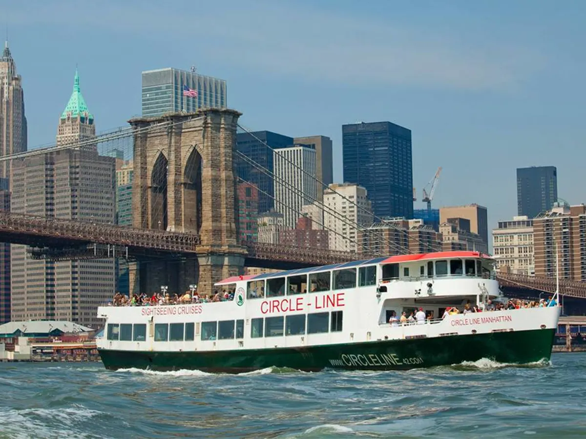 Circle Line Sightseeing-Schiff fährt auf dem East River in New York mit der Brooklyn Bridge und Skyline im Hintergrund.