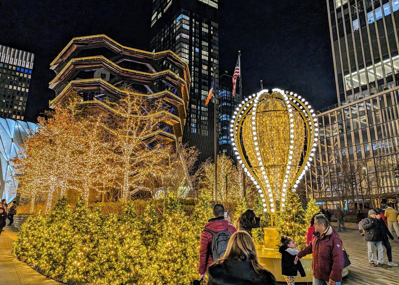 Golden beleuchtete Weihnachtsbäume und festliche Lichtdekoration vor der Aussichtsstruktur The Vessel in Hudson Yards, New York.