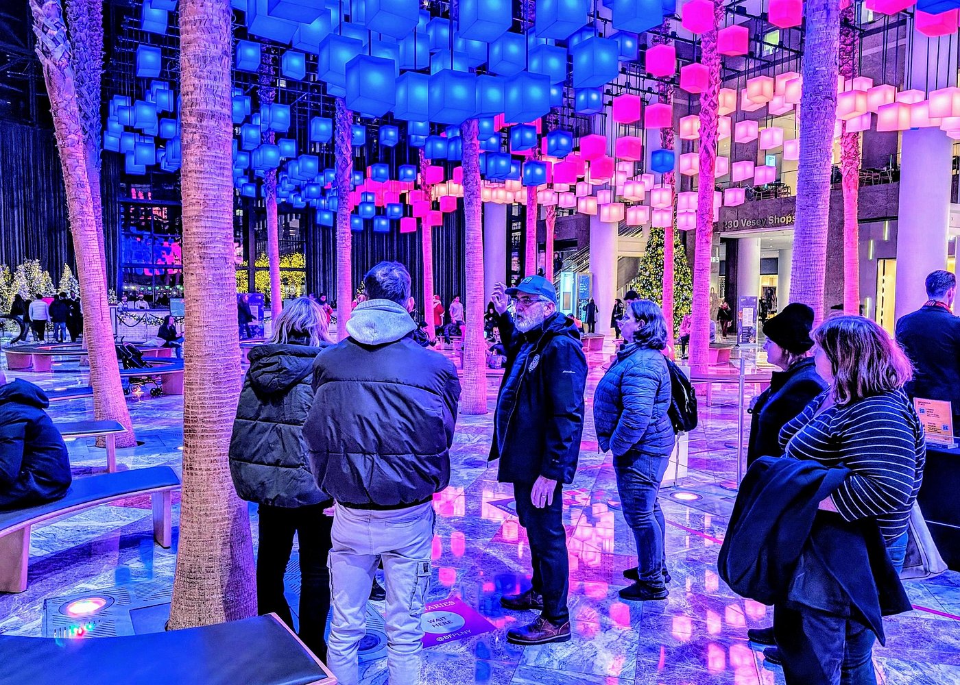 Besucher unter einer Installation aus blau und rosa leuchtenden Würfeln im Brookfield Place in Lower Manhattan.
