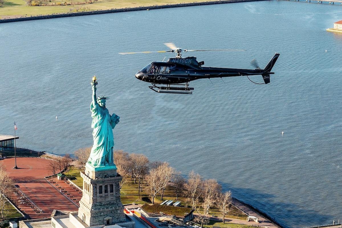 Schwarzer Helikopter fliegt über die Freiheitsstatue mit New Yorker Hafen im Hintergrund