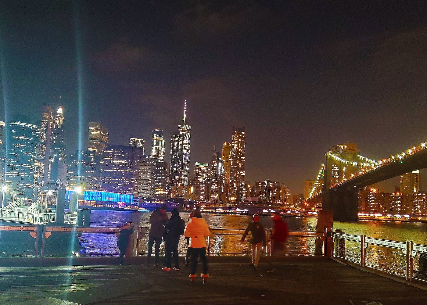 Blick von Brooklyn auf die beleuchtete Skyline von Manhattan und die Brooklyn Bridge bei Nacht.