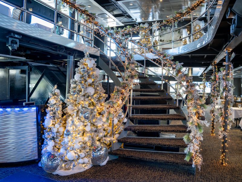Festlich dekorierter Innenbereich eines City-Cruises-Schiffes mit geschmückten Weihnachtsbäumen, Lichterketten und geschwungener Treppe.