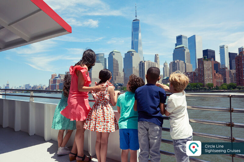 Kinder auf einem Sightseeing-Boot der Circle Line mit Blick auf die Skyline von Manhattan und das One World Trade Center.