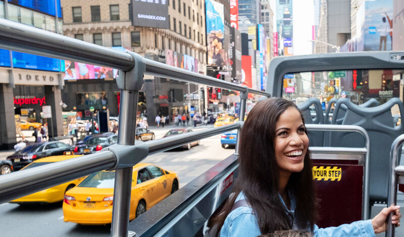 Besucherin im offenen Oberdeck eines Big Bus Sightseeing-Busses bei einer Stadtrundfahrt durch den Times Square in New York.