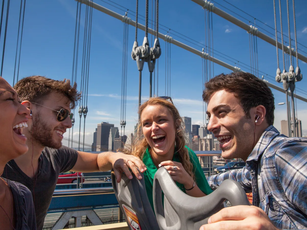 Vier Freunde lachen auf der Brooklyn Bridge mit Blick auf die Skyline von Lower Manhattan