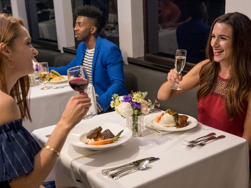 Lachende Gäste stoßen mit Rotwein und Sekt am festlich gedeckten Tisch der Dinner Cruise an
