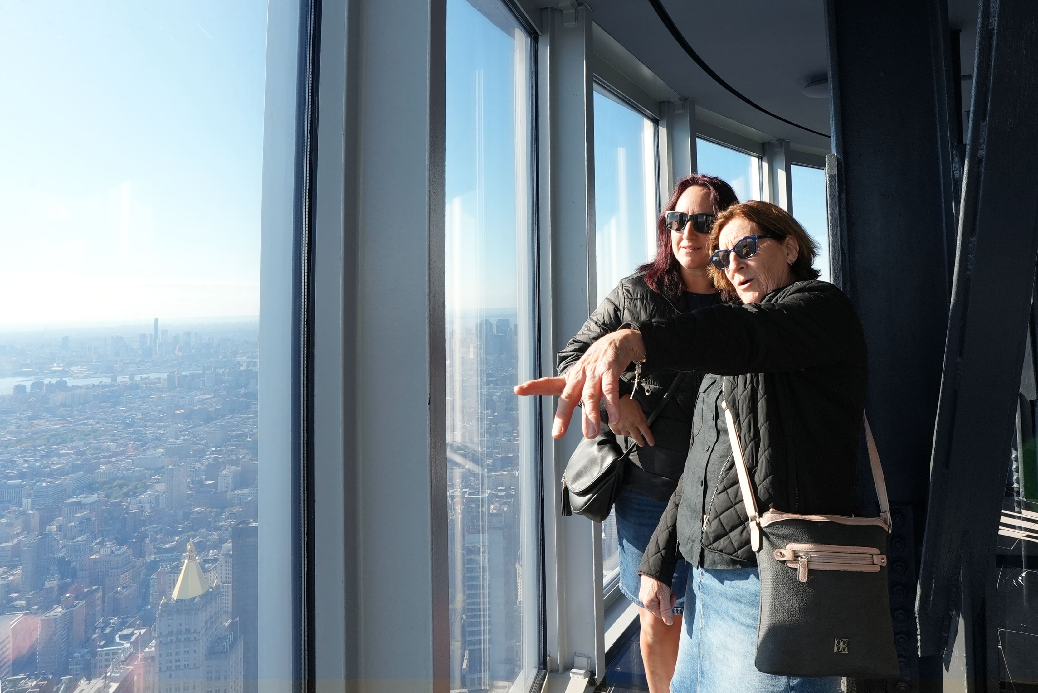 Zwei Frauen zeigen auf die Skyline von Manhattan und genießen die Aussicht vom Empire State Building in New York.