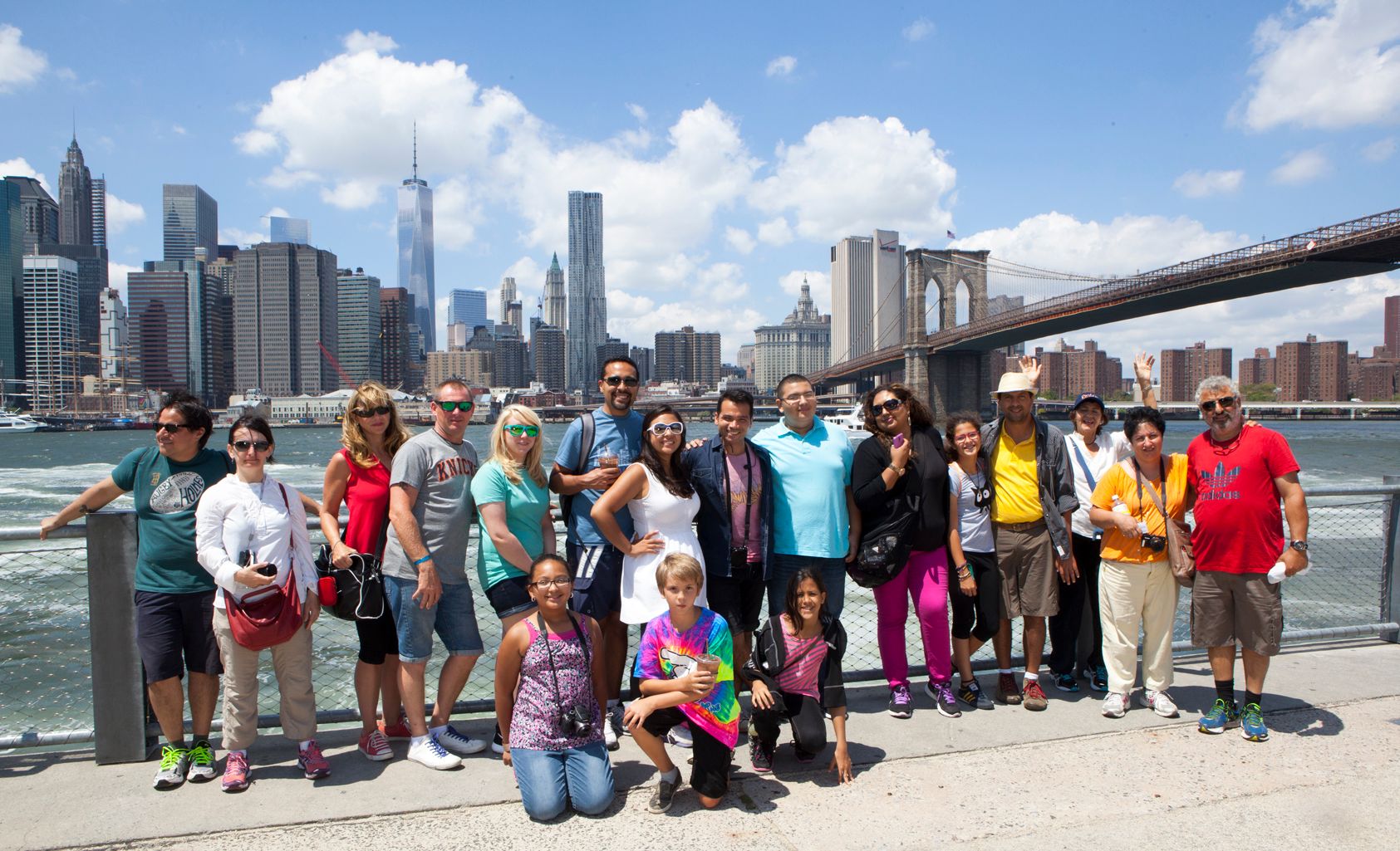 Eine große Touristen-Gruppe posiert für ein Erinnerungsfoto am Ufer mit Blick auf die New Yorker Skyline und die Brooklyn Bridge.