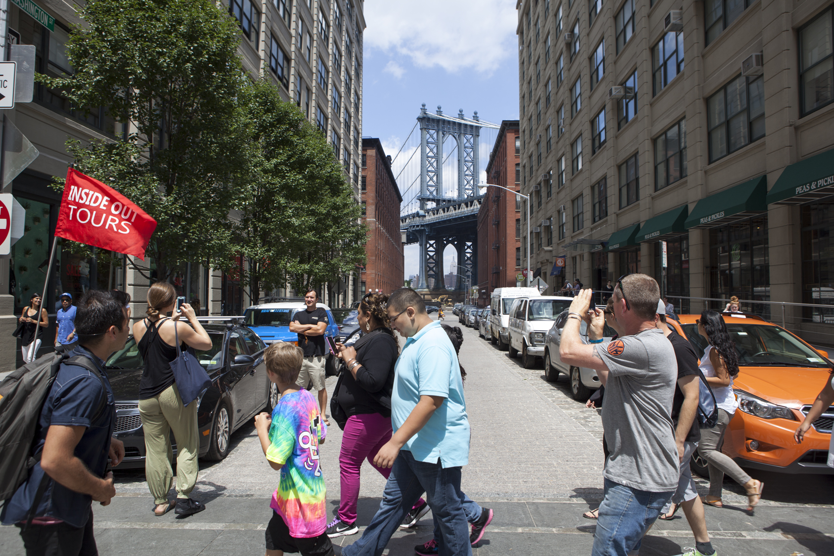 Touristen und Passanten fotografieren und flanieren auf einer belebten Straße in DUMBO mit Blick auf die Manhattan Bridge.