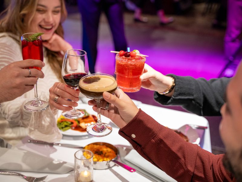Gäste stoßen mit Cocktails und Wein an einem gedeckten Tisch während einer Dinner Cruise in New York an.