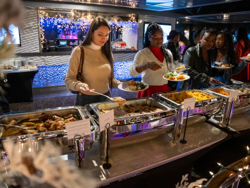 Gäste bedienen sich an einem reichhaltigen Dinner-Buffet mit verschiedenen warmen Speisen während einer Schifffahrt.