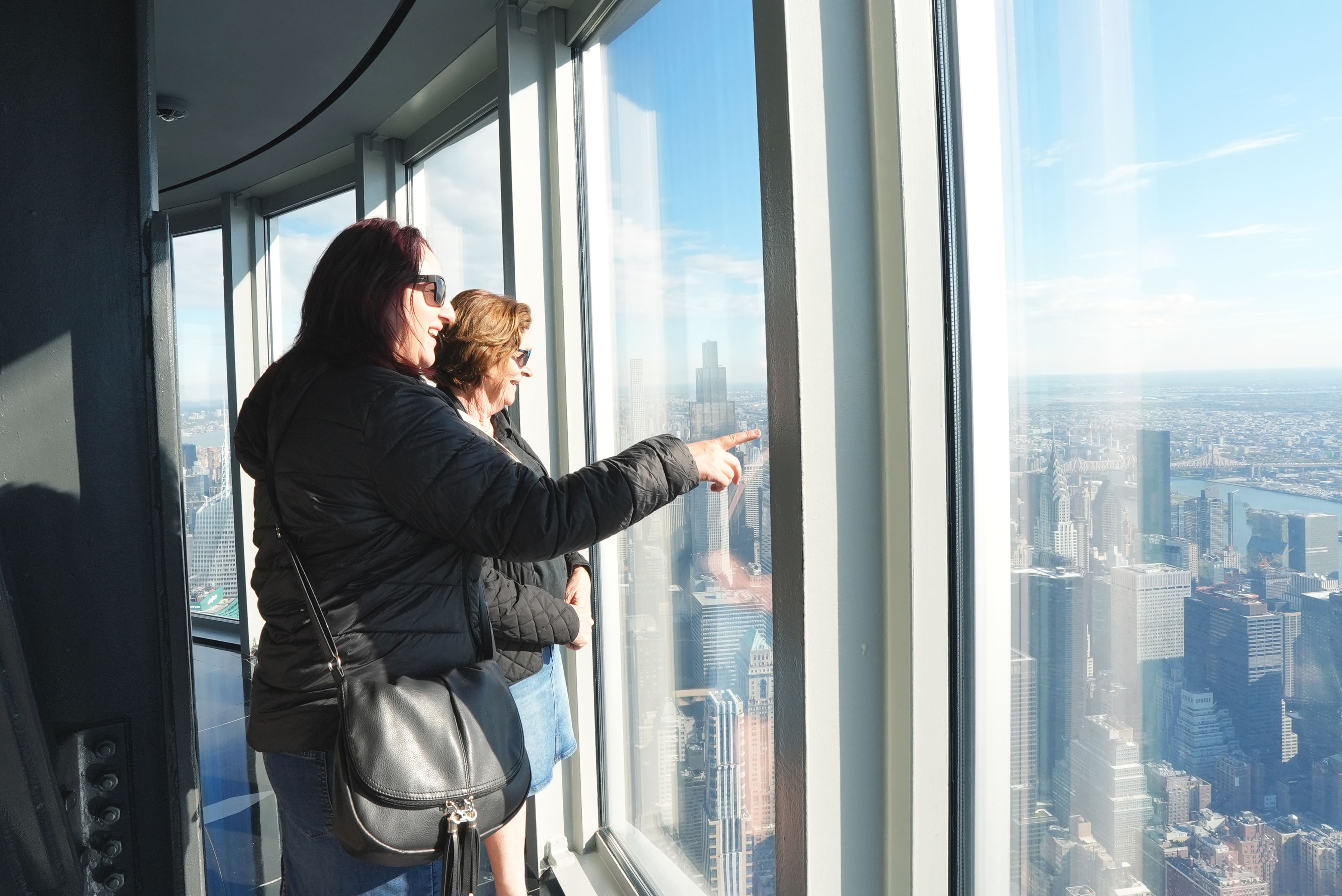 Zwei Besucherinnen genießen durch die Panoramafenster den weiten Blick über Manhattan vom Empire State Building.