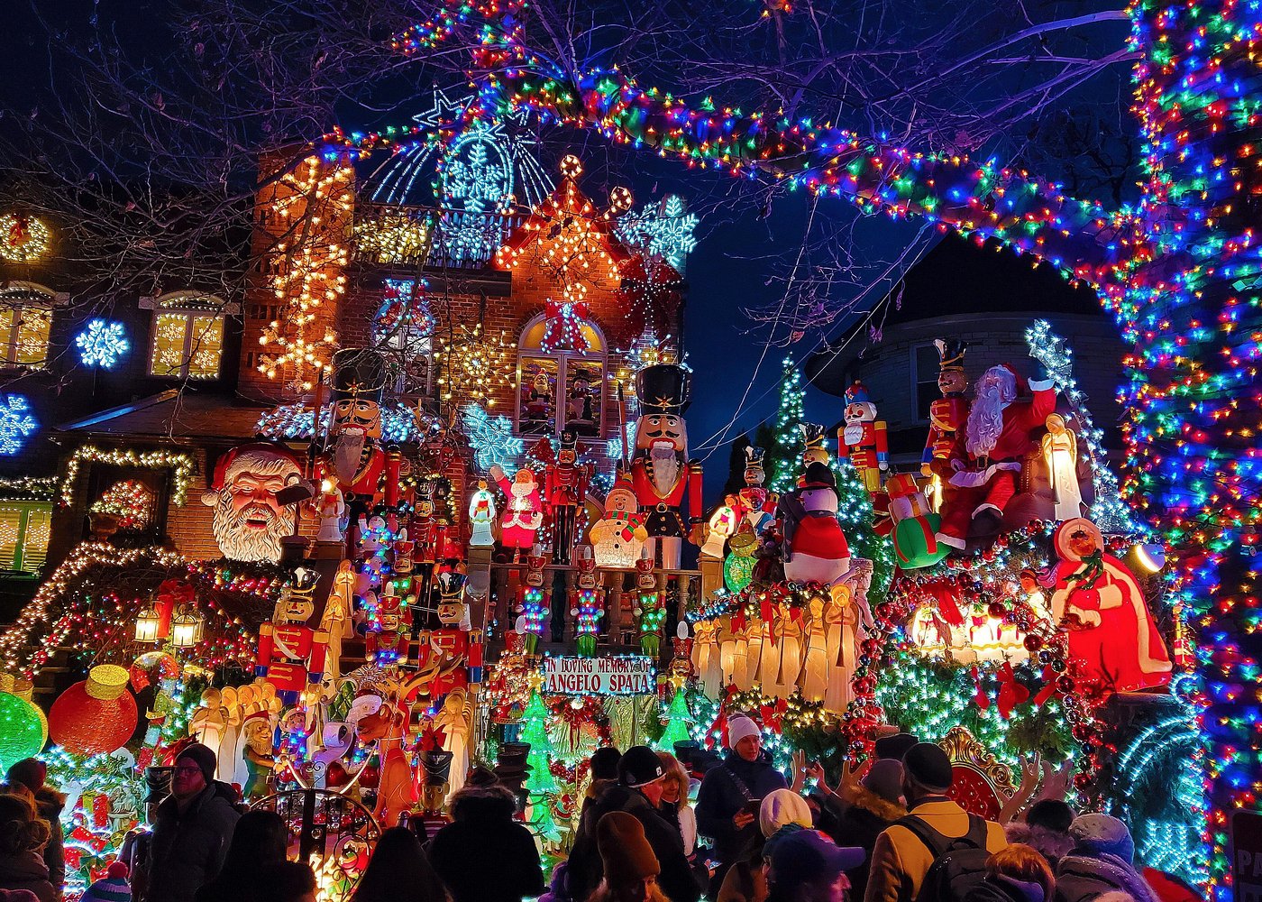 Zahlreiche Besucher bewundern ein festlich beleuchtetes Haus in Dyker Heights mit Nussknackern, Weihnachtsfiguren und bunten Lichtern.