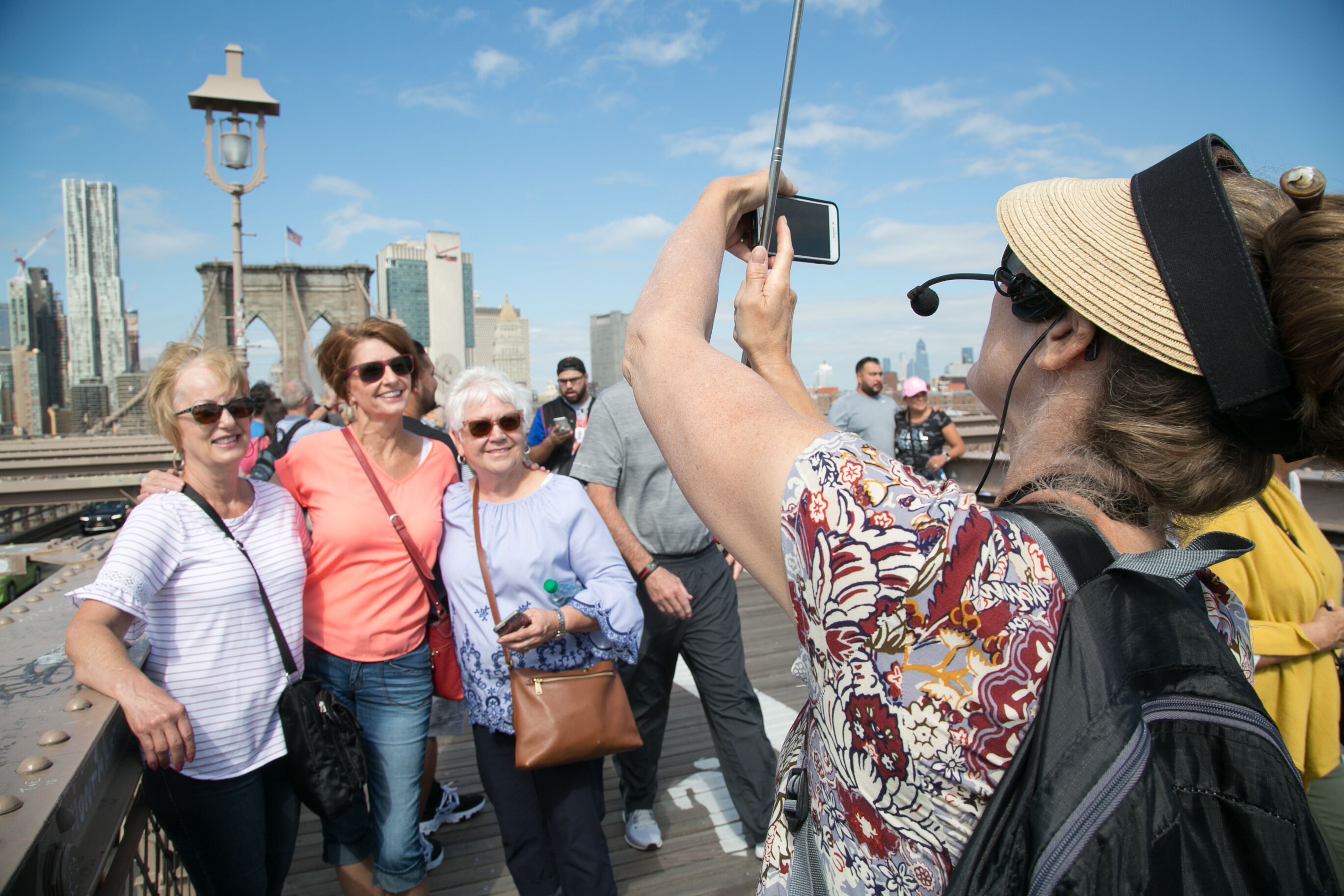 Eine Reiseleiterin macht ein Selfie mit einer Gruppe gut gelaunter Touristen auf der Brooklyn Bridge vor der Skyline von New York.