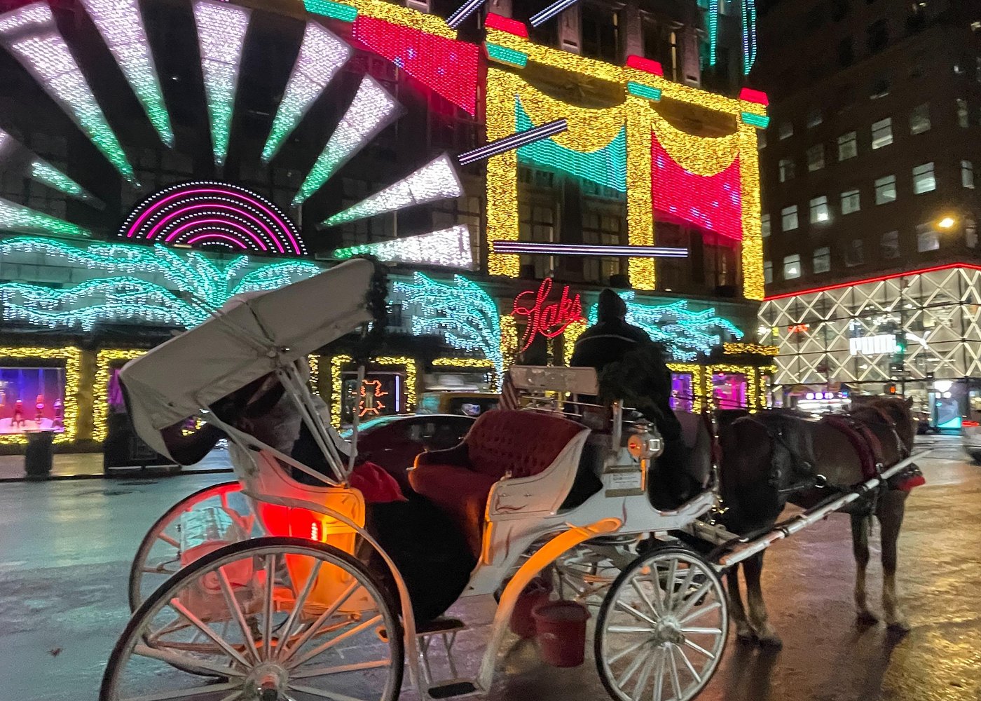 Weiße Pferdekutsche vor der farbenprächtigen Weihnachtsbeleuchtung des Kaufhauses Saks Fifth Avenue in Manhattan.